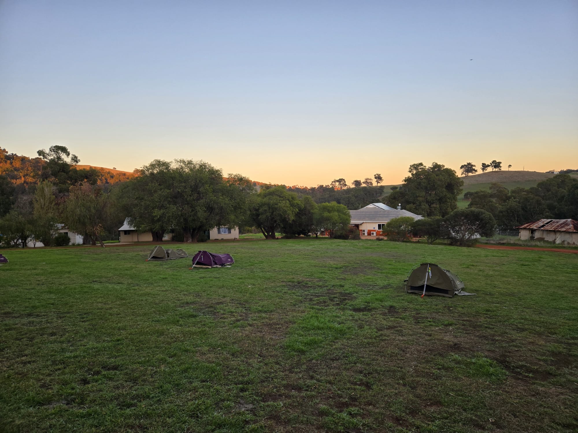 A canvas swag set up for camping on a grassy area at Roelands Village, with trees in the background.